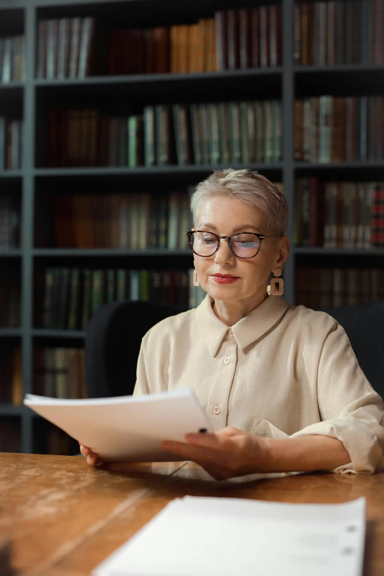Elderly woman reviewing documents in a library setting, symbolizing wisdom and learning.